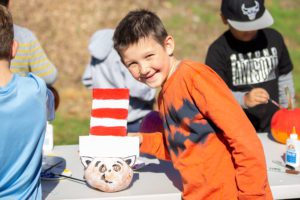 student stands next to cat in the hat decorated pumpkin