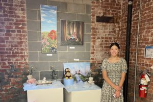 student stands with her paintings at exhibit