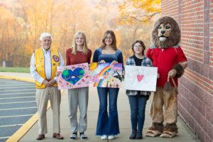 students hold posters next to lion mascot