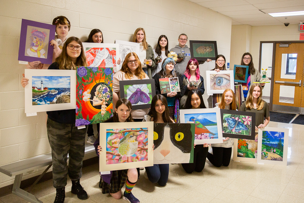 students stand with their artwork in a school hallway