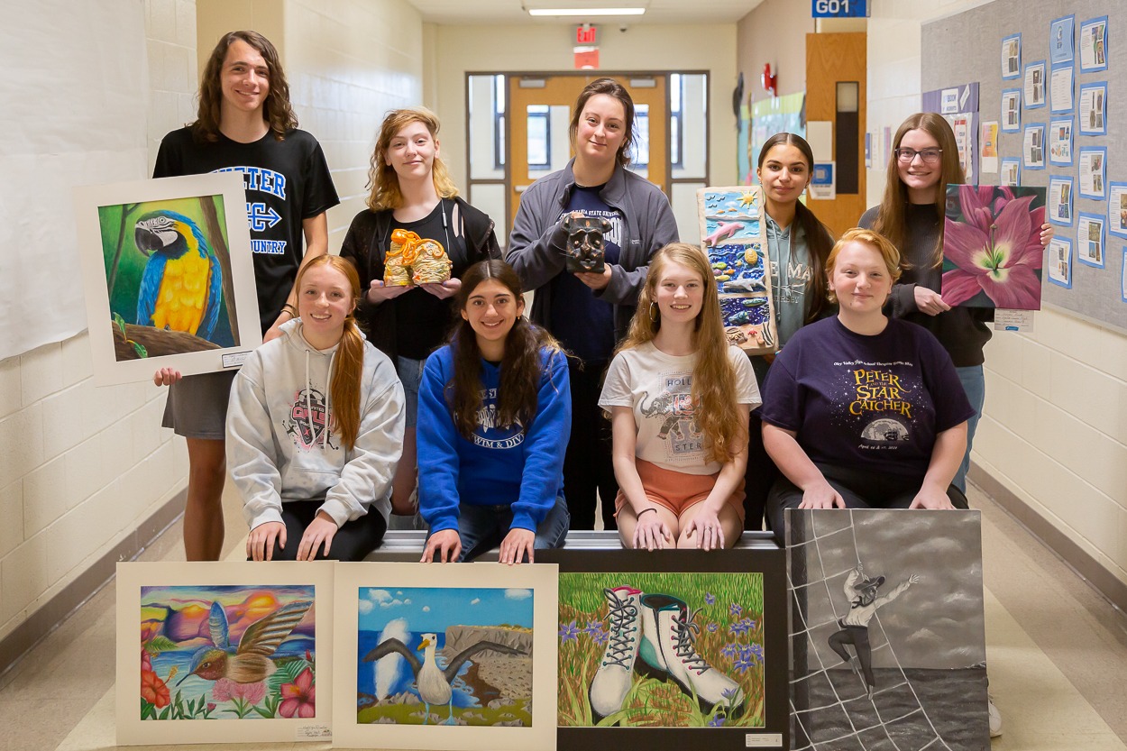 students stand in a hallway holding artwork they created