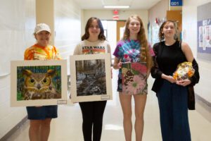 students stand in a hallway holding artwork they created