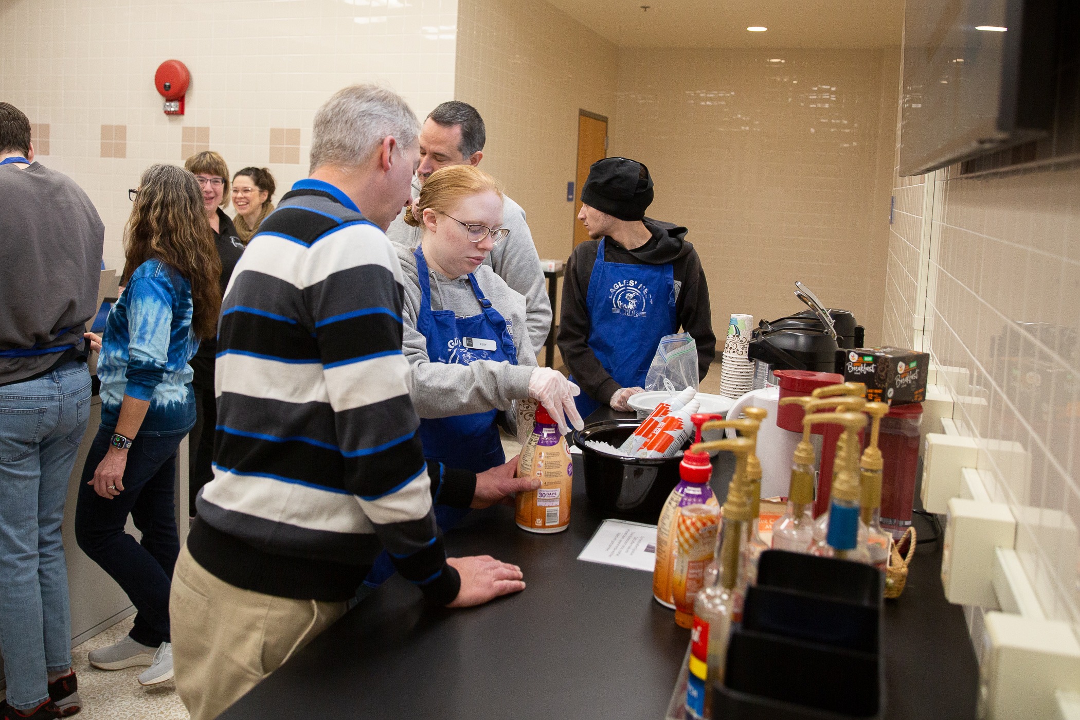 student puts creamer into a coffee cup with teacher's help