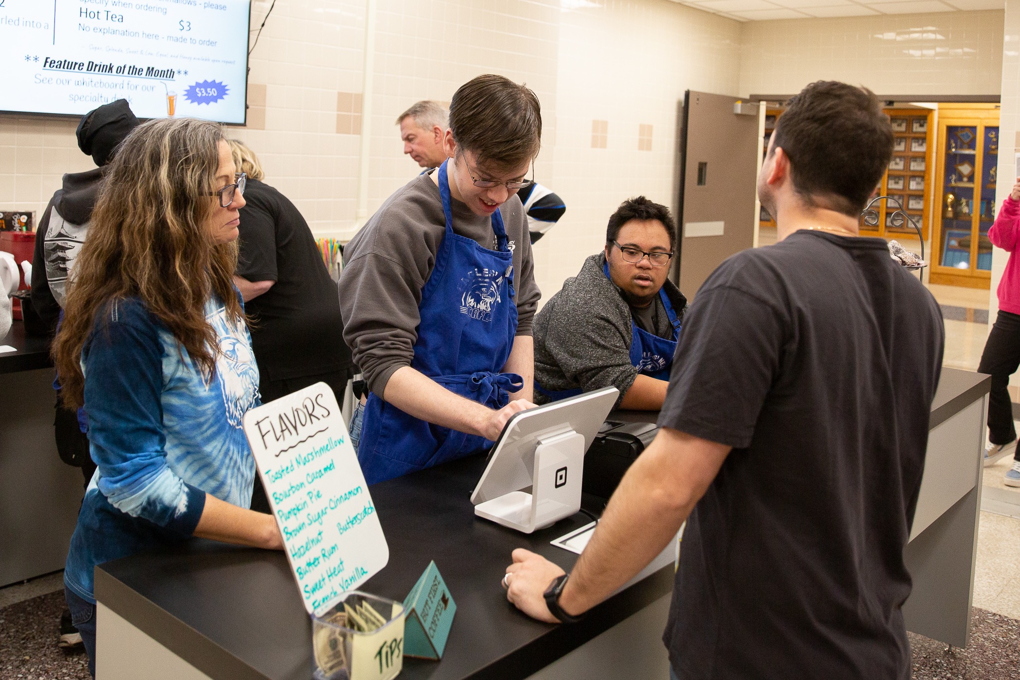 student uses a pos system while a teacher overlooks his work