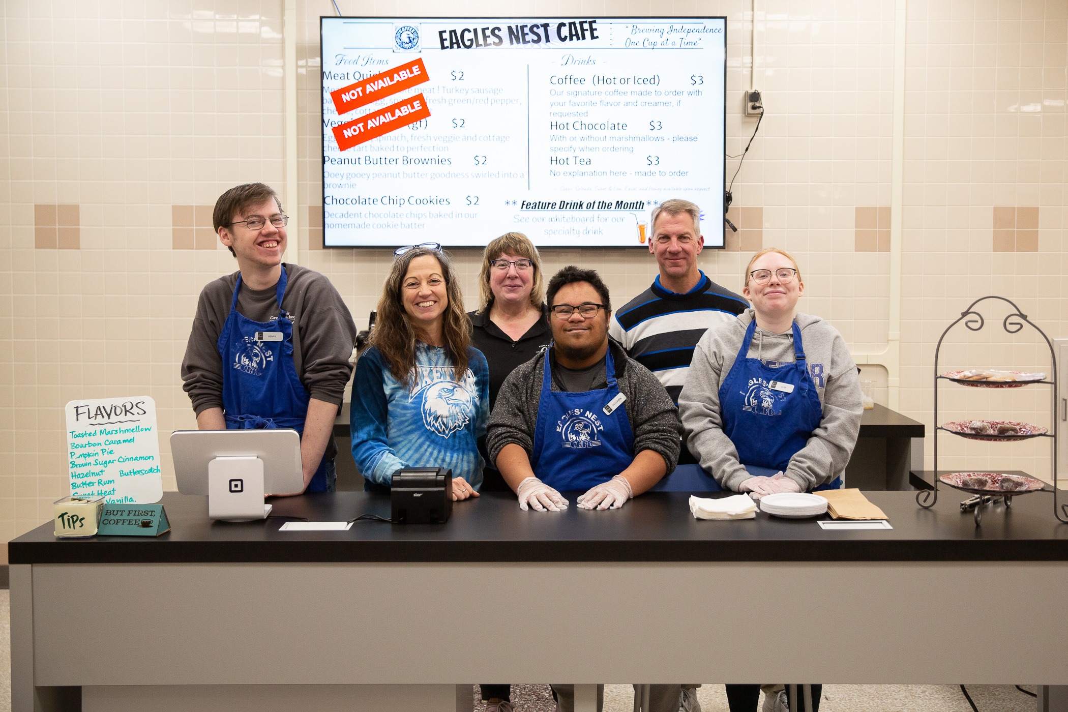 students stand behind a counter with a menu above them