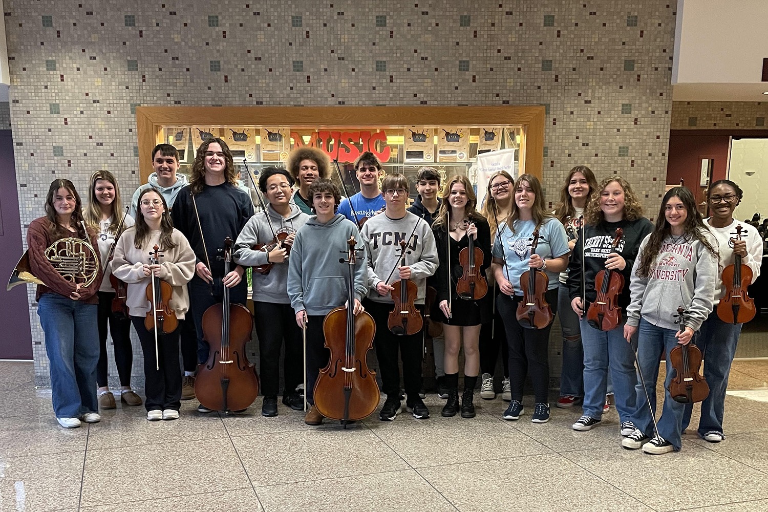 a group of students hold string instruments in a hallway